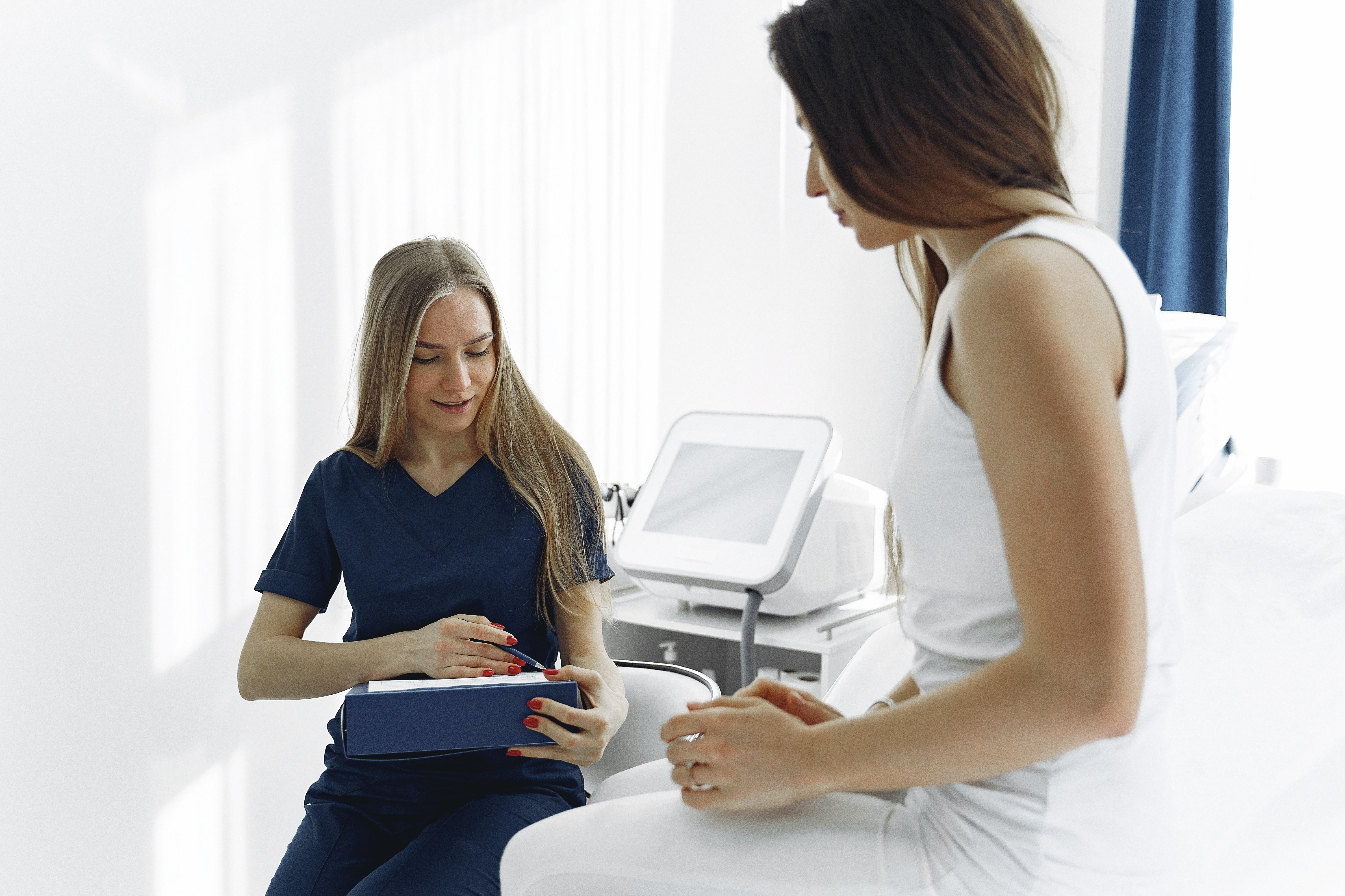 A young woman wearing white clothing is visiting with a medical professional.