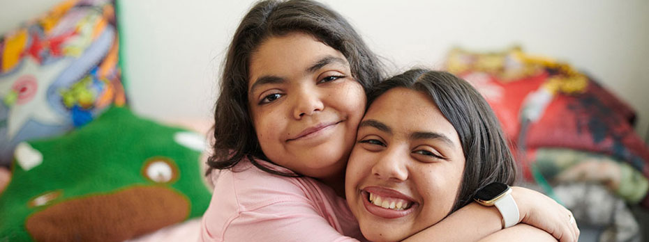 A brother and sister hug on a couch in the living room.