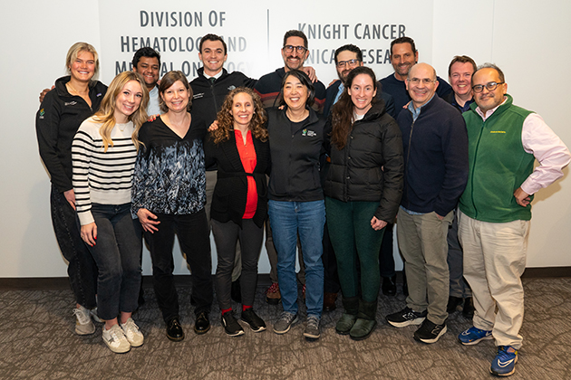 A group photo of the GI cancer research group. There are 14 men and women standing in front of their office space at OHSU.