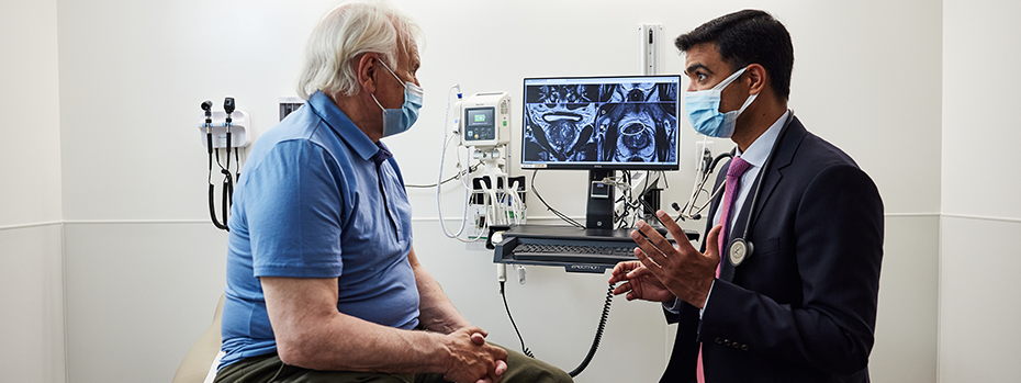 A doctor and patient talk in an exam room next to a monitor showing digital images.